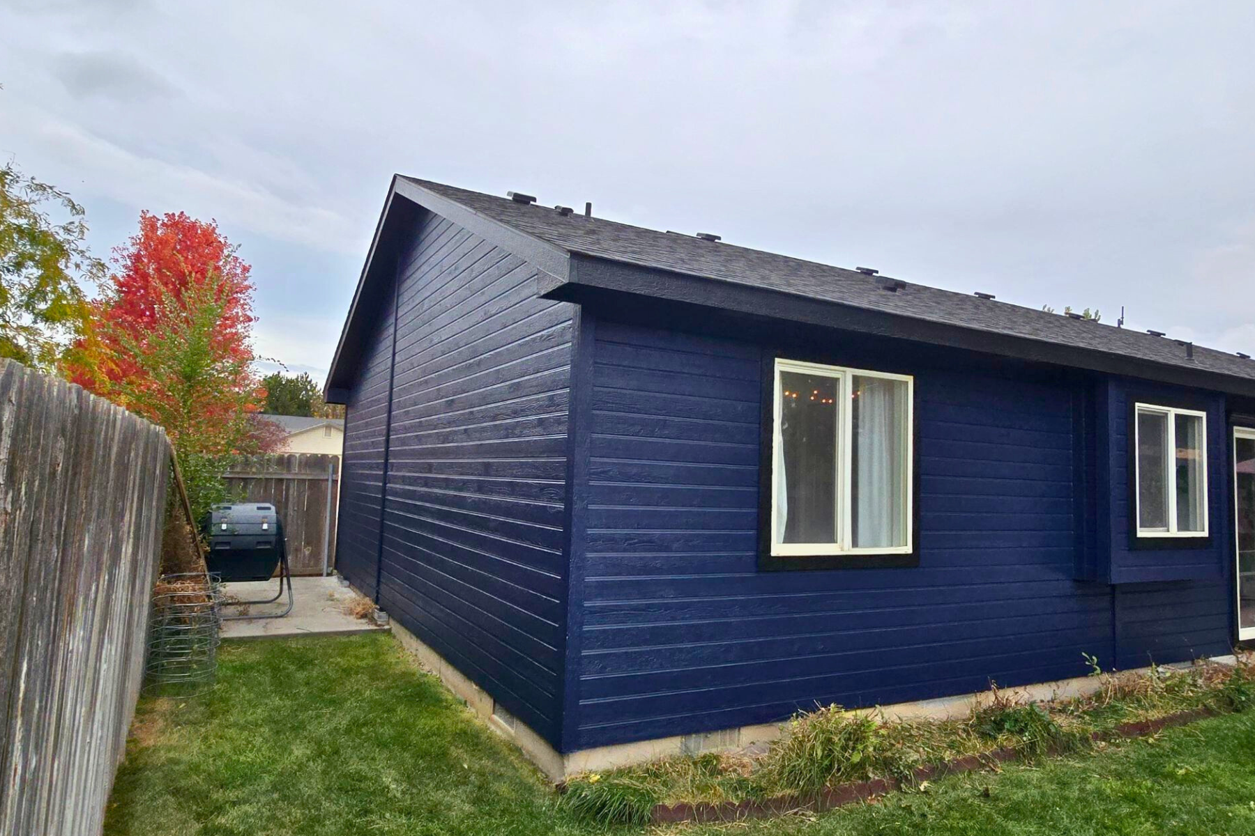 A blue house with a fence and a grill in the backyard.