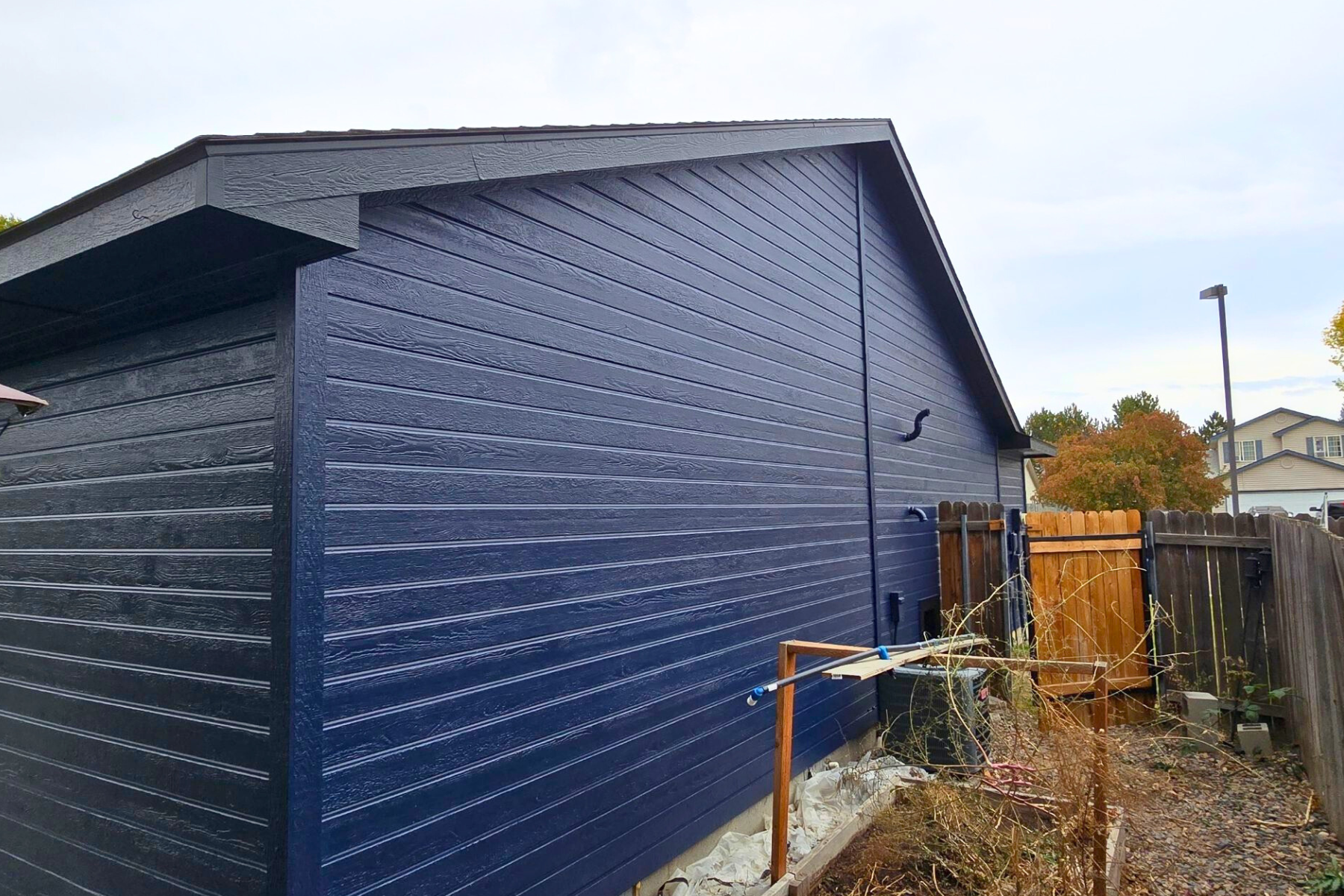A blue garage with a wooden fence in the backyard.