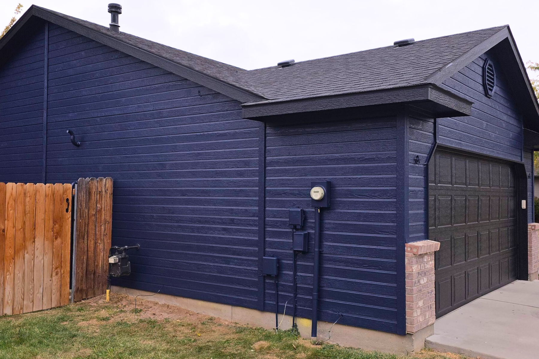 A blue house with a black garage door and a wooden fence.