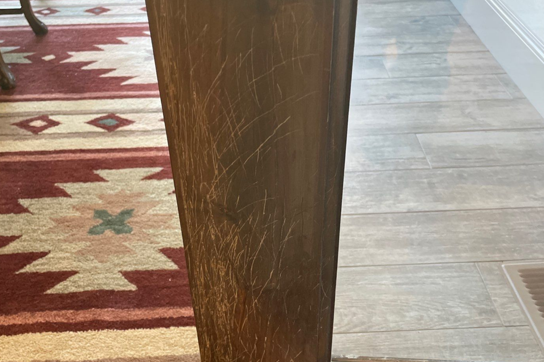 A wooden table leg is sitting on a wooden floor next to a rug.