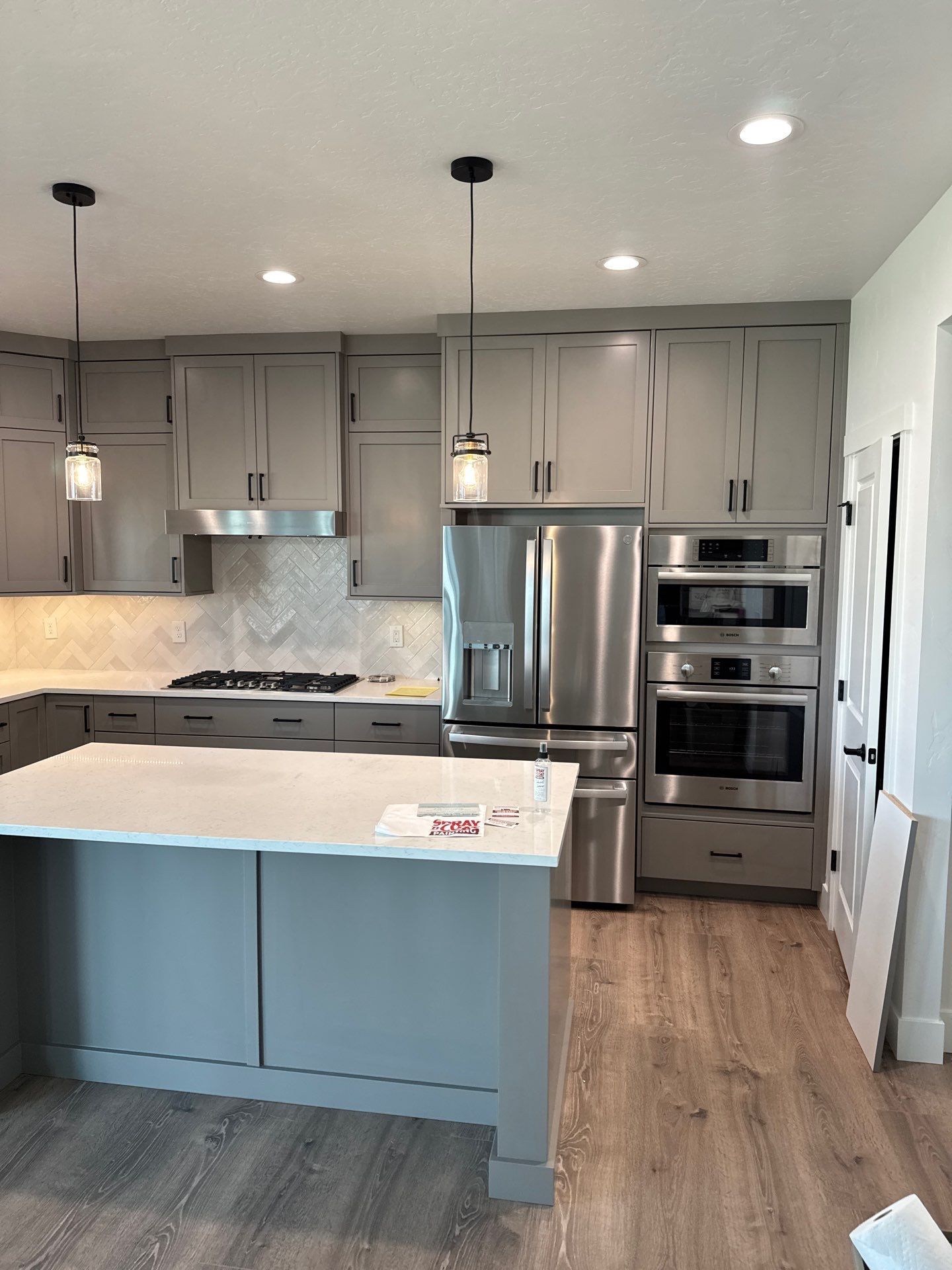 Modern kitchen with gray cabinets, blue island, stainless steel appliances, and wood floor