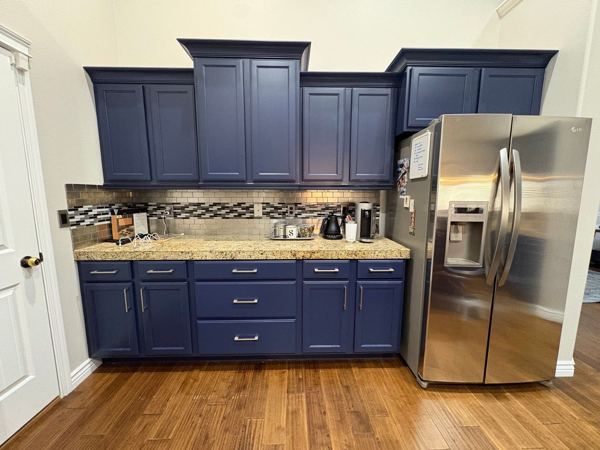 Modern kitchen with navy cabinets, beige countertop, and stainless steel refrigerator on wood floor