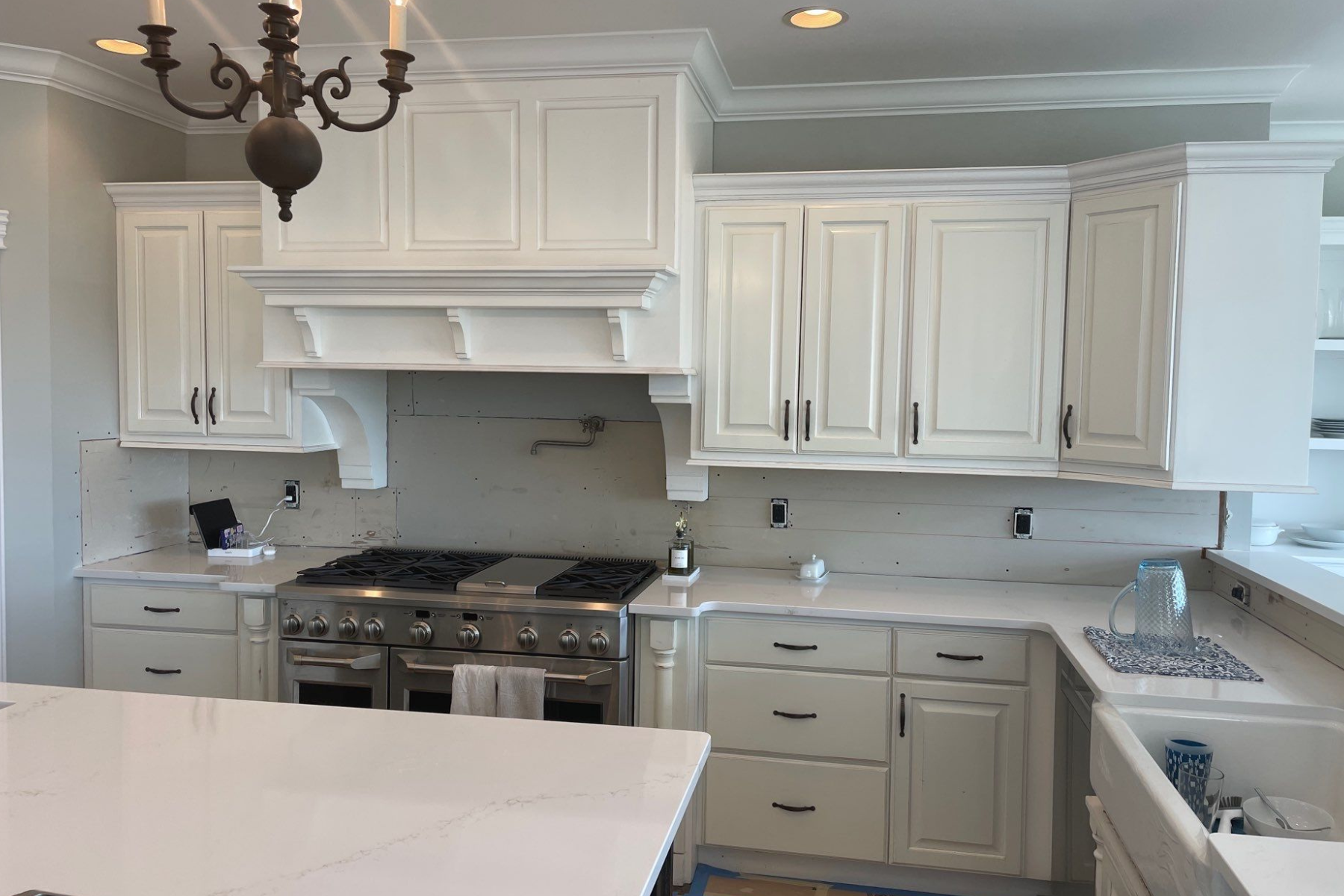 A kitchen with white cabinets , a stove , a sink , and a chandelier.