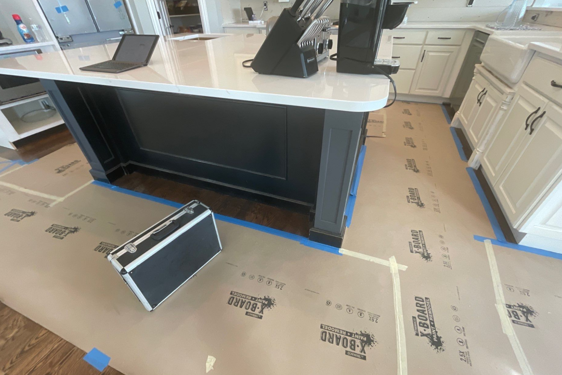 A black briefcase is sitting on the floor in a kitchen.