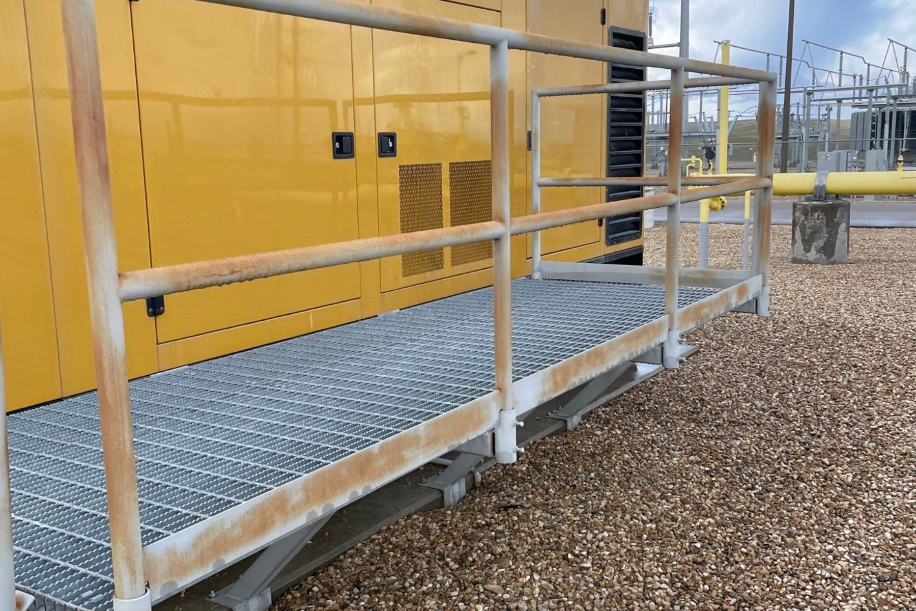 A metal walkway with a railing leading to a yellow building