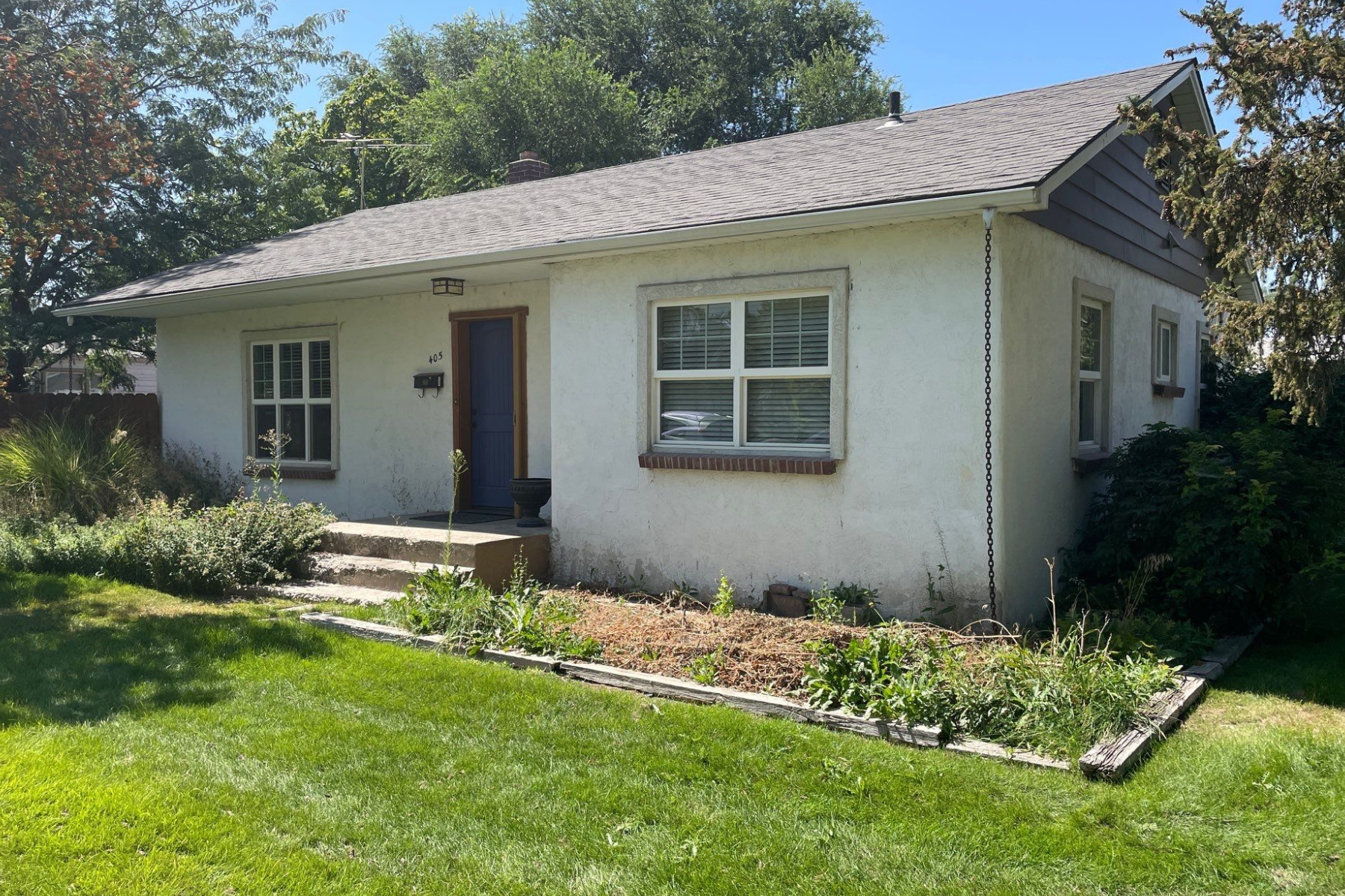 A small white house with a gray roof is sitting on top of a lush green lawn.