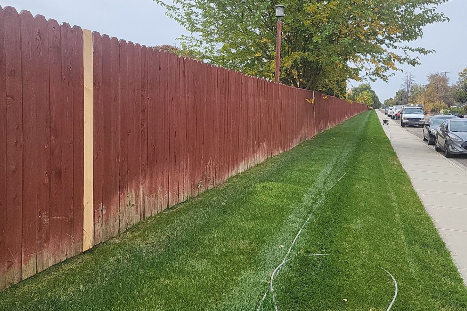 A red wooden fence is sitting next to a lush green lawn.