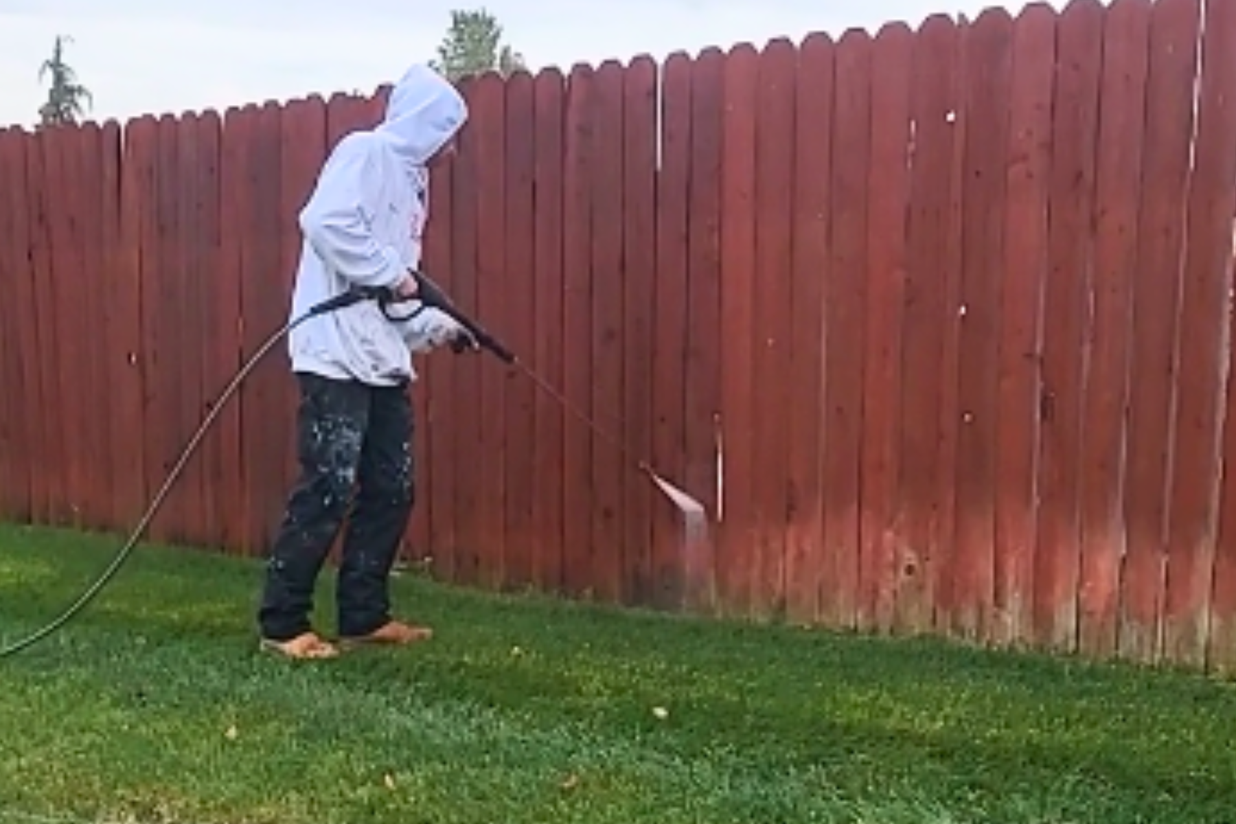 A man is cleaning a red wooden fence with a pressure washer.