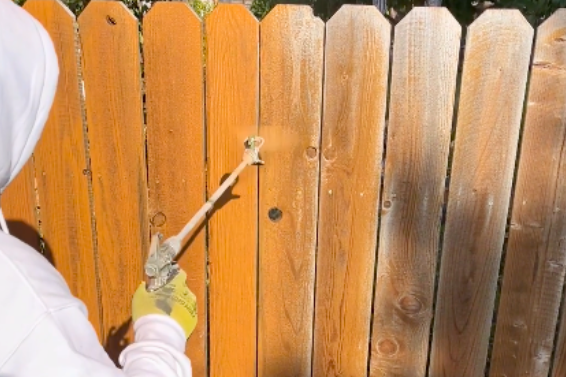 A person is painting a wooden fence with a sprayer.