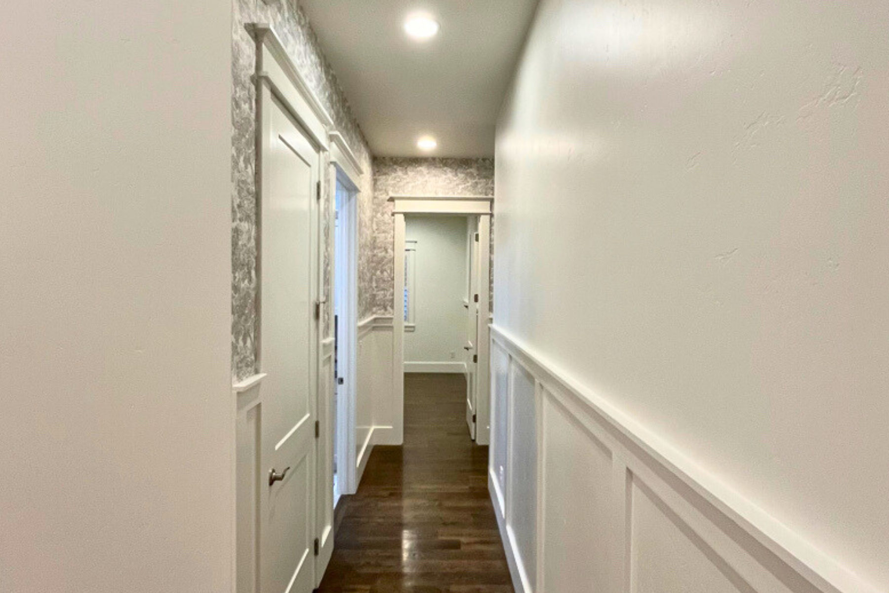 A long hallway with white walls and wooden floors in a house.