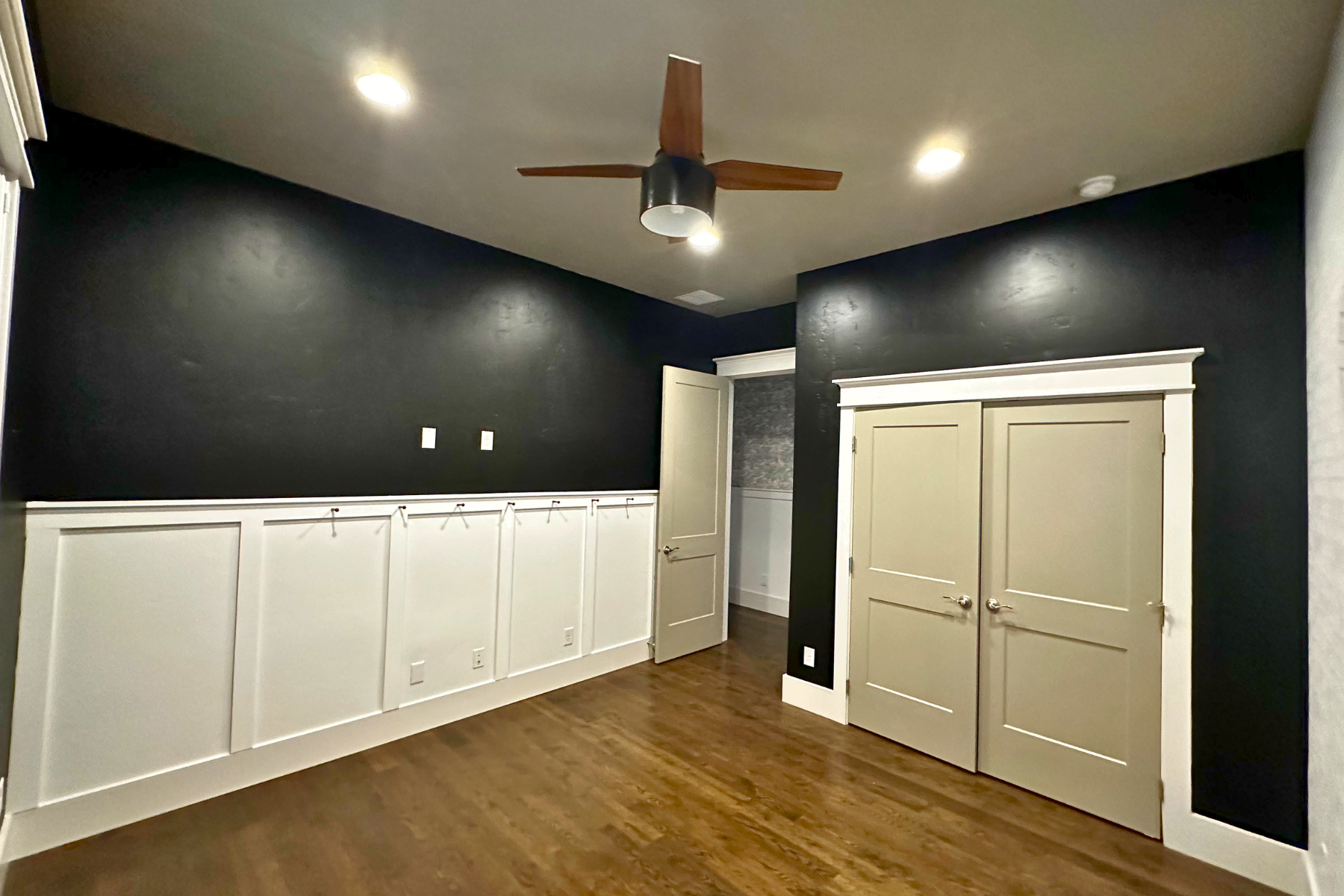 An empty room with black walls and a ceiling fan.