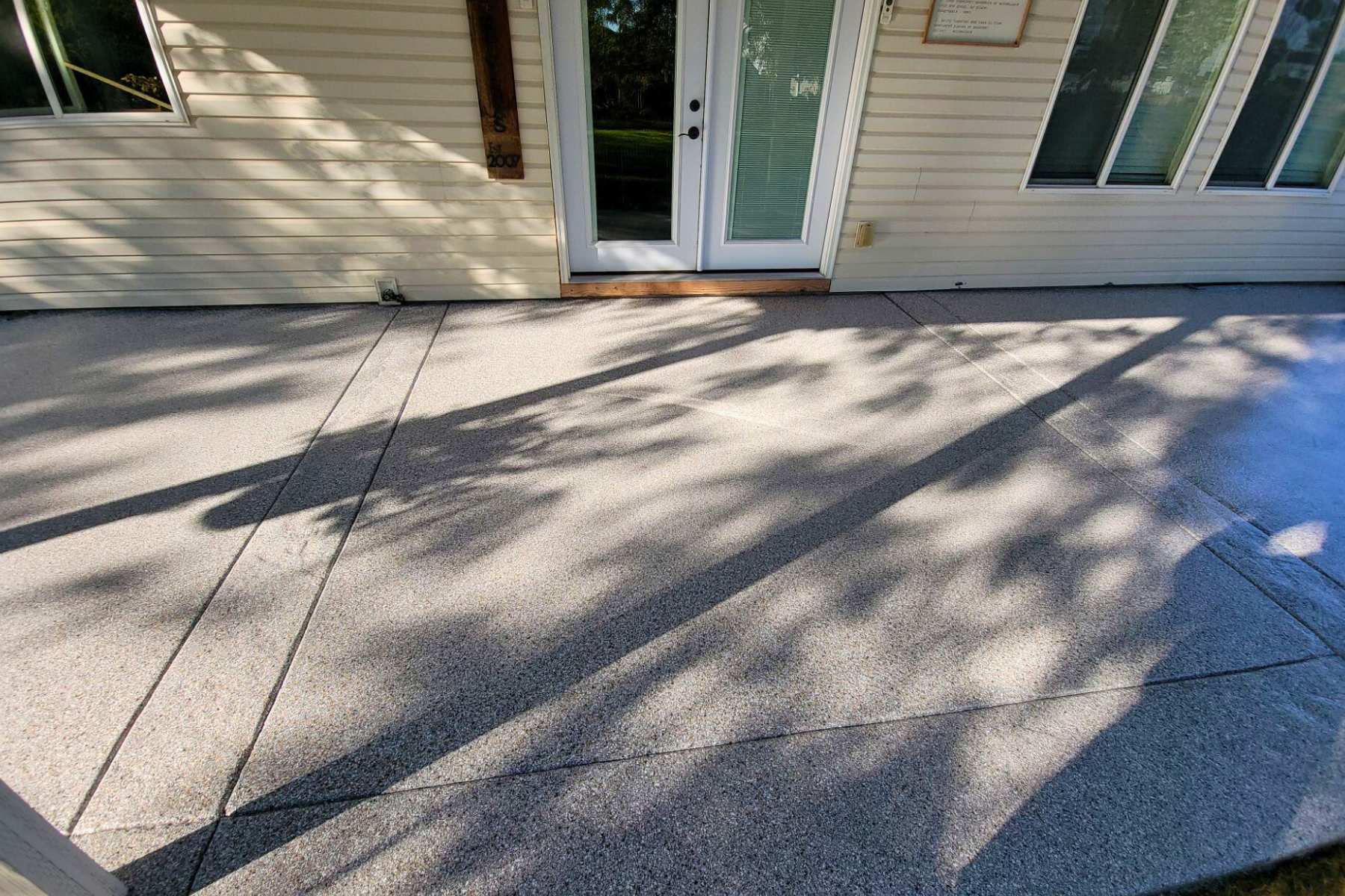A concrete patio in front of a house with trees casting shadows on it.