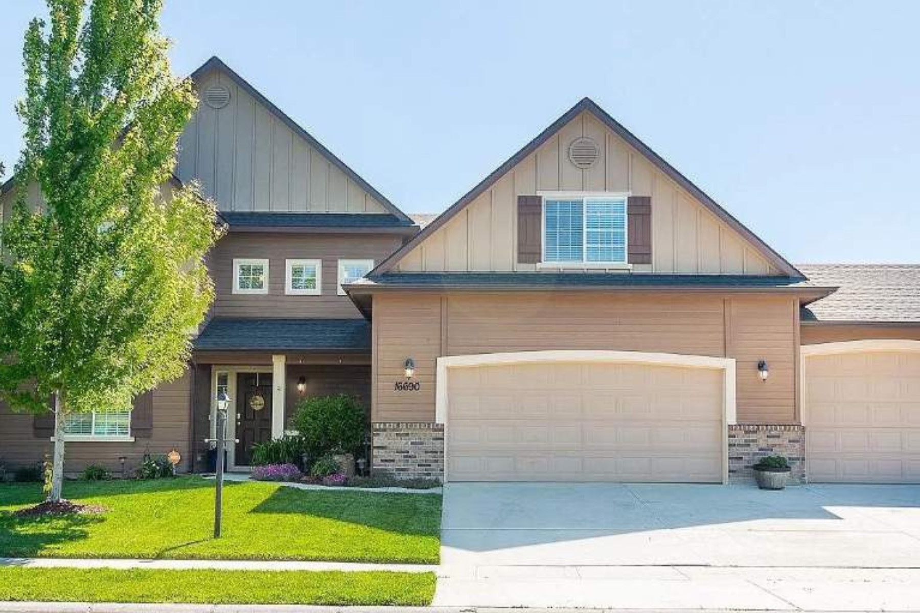 A large house with two garage doors and a tree in front of it