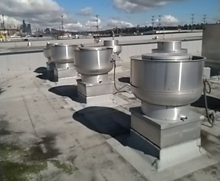 A row of stainless steel exhaust fans on the roof of a building A row of stainless steel exhaust fans on the roof of a building
