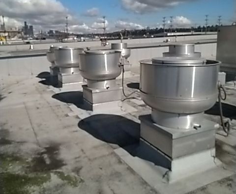 A row of stainless steel exhaust fans on the roof of a building A row of stainless steel exhaust fans on the roof of a building