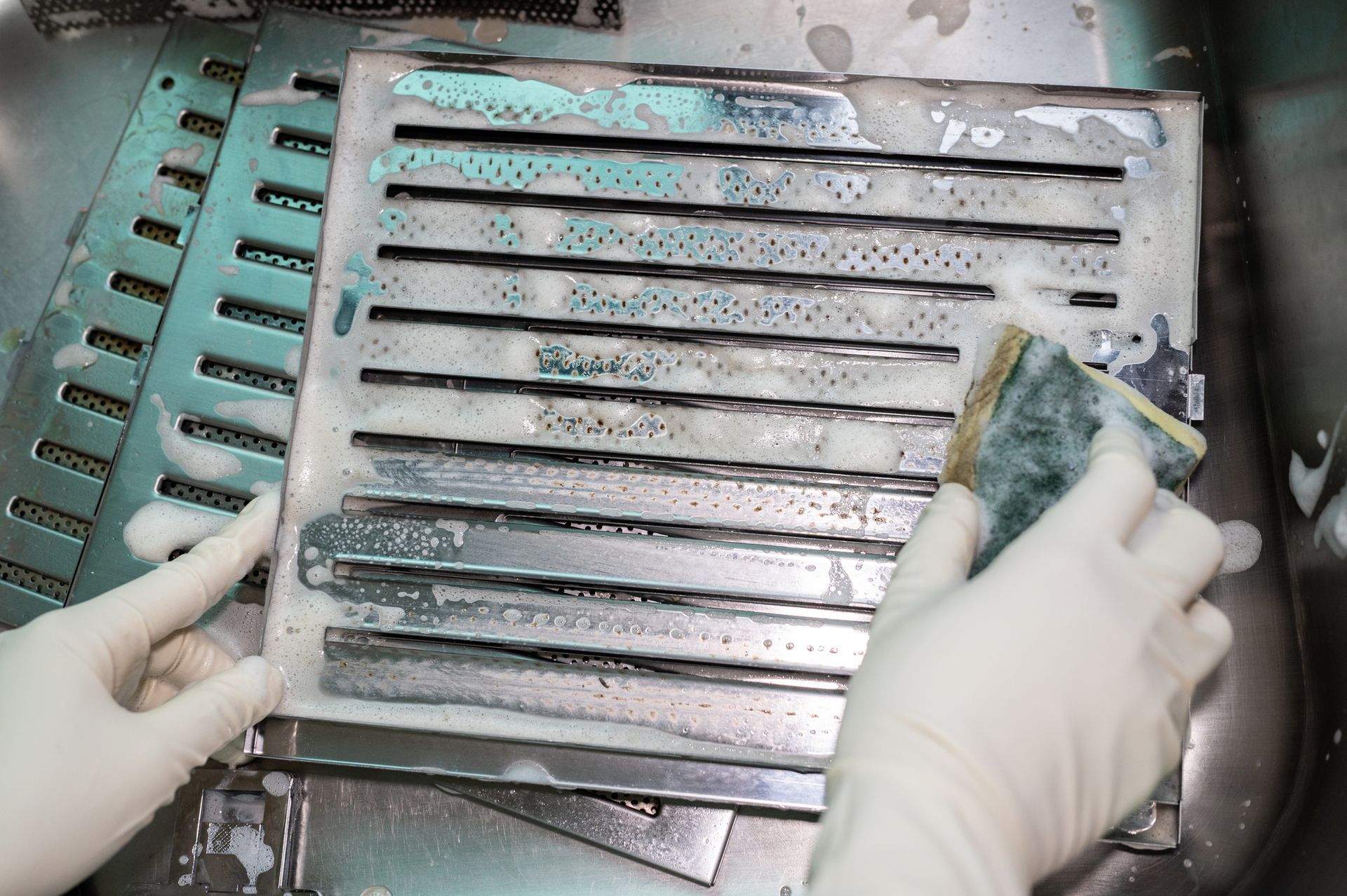 Someone is using a scrub sponge to clean a dirty cooker hood filter.