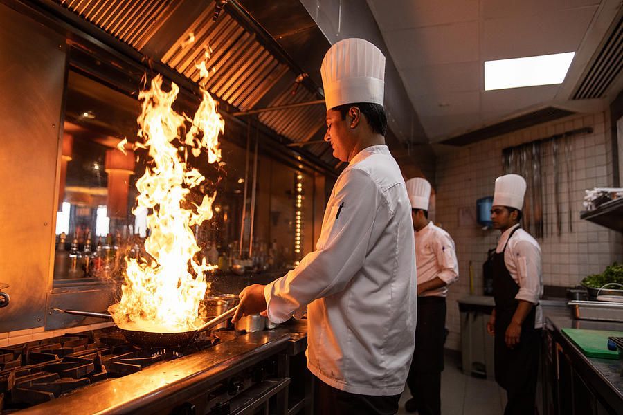 A chef is cooking food in a kitchen with flames coming out of a pan. A chef is cooking food in a kitchen with flames coming out of a pan.