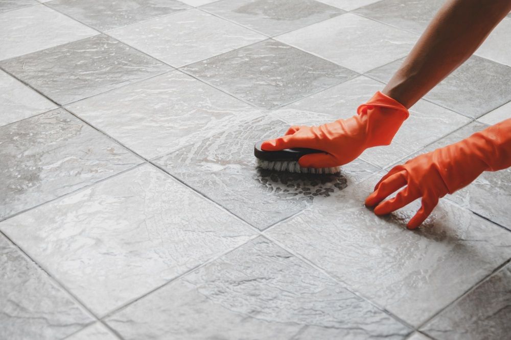 Person Wearing Orange Gloves Scrubbing Grey Tiled Floor — David Son Tiling in Springdale Heights, NSW