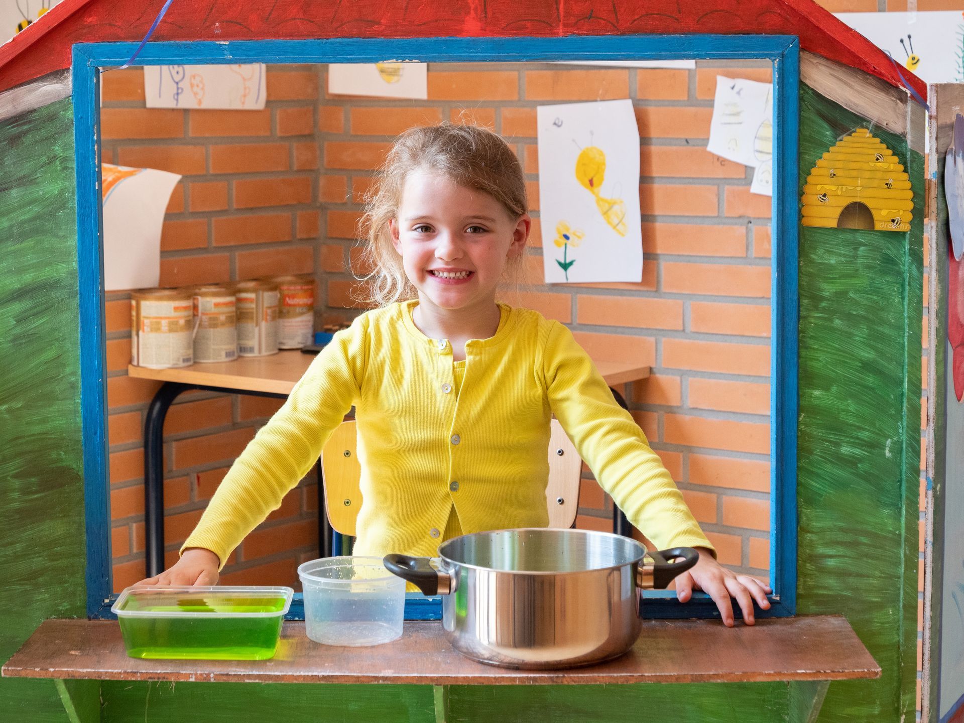 Een klein meisje in een gele trui staat voor een speelhuisje.