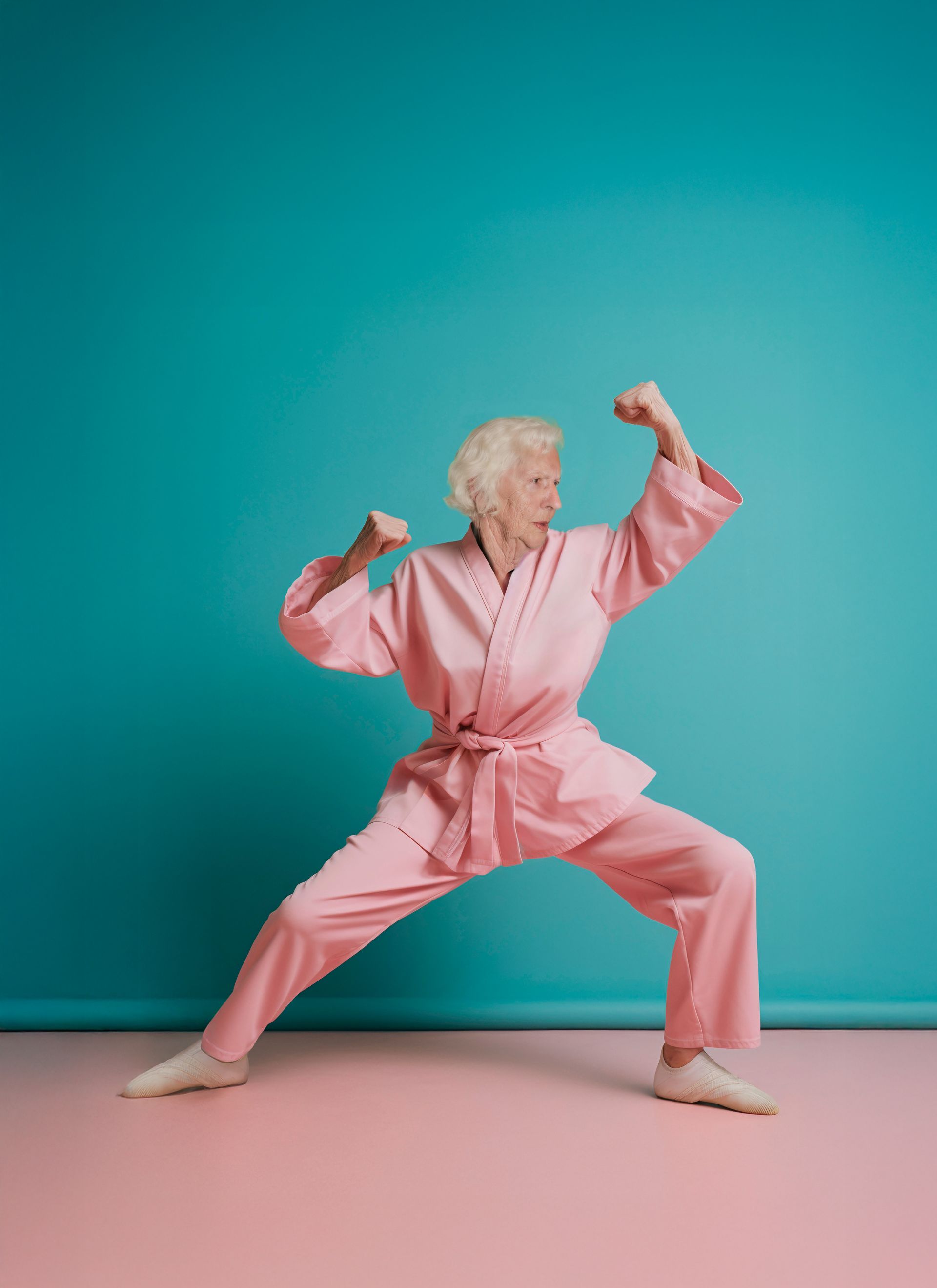 Een persoon in een roze vechtsportpak staat in een krachtige houding tegen een turquoise muur, met beide vuisten in de lucht.