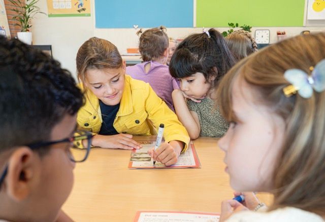 Een groep kinderen zit aan een tafel in een klaslokaal.