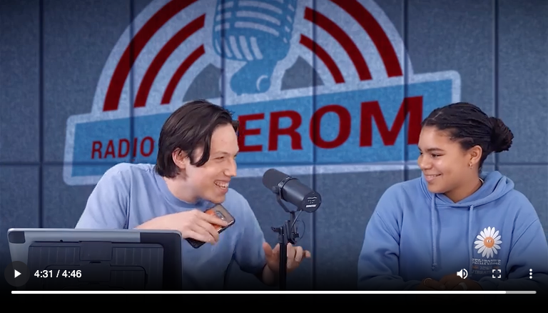 Een man en een vrouw praten voor een bord met de tekst radio erom