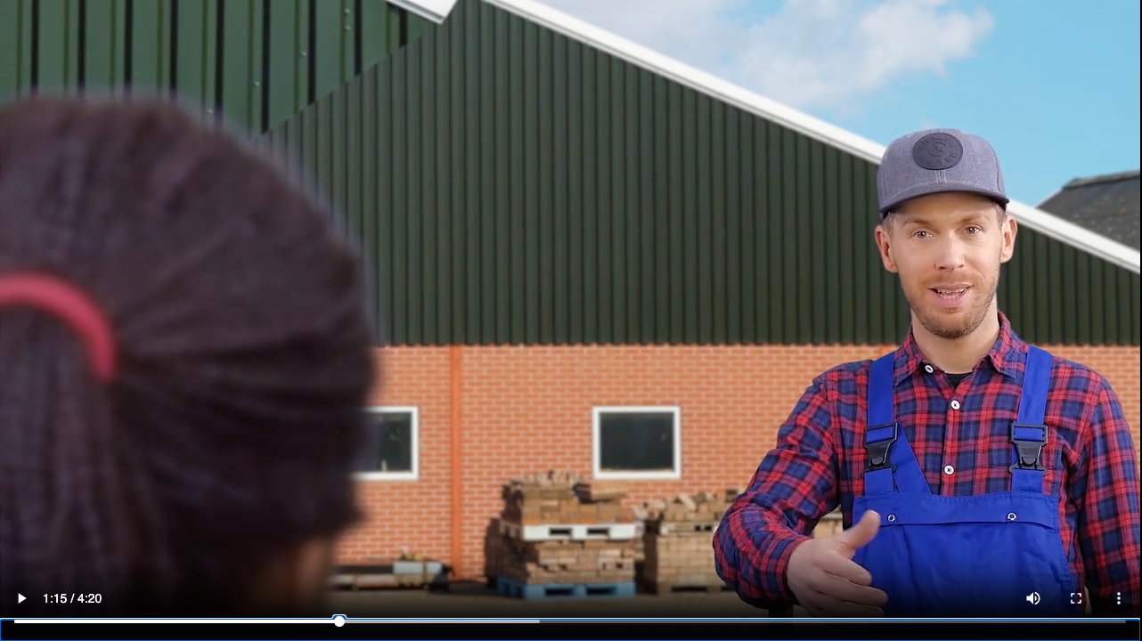 Een man in een overall praat met een vrouw voor een gebouw.