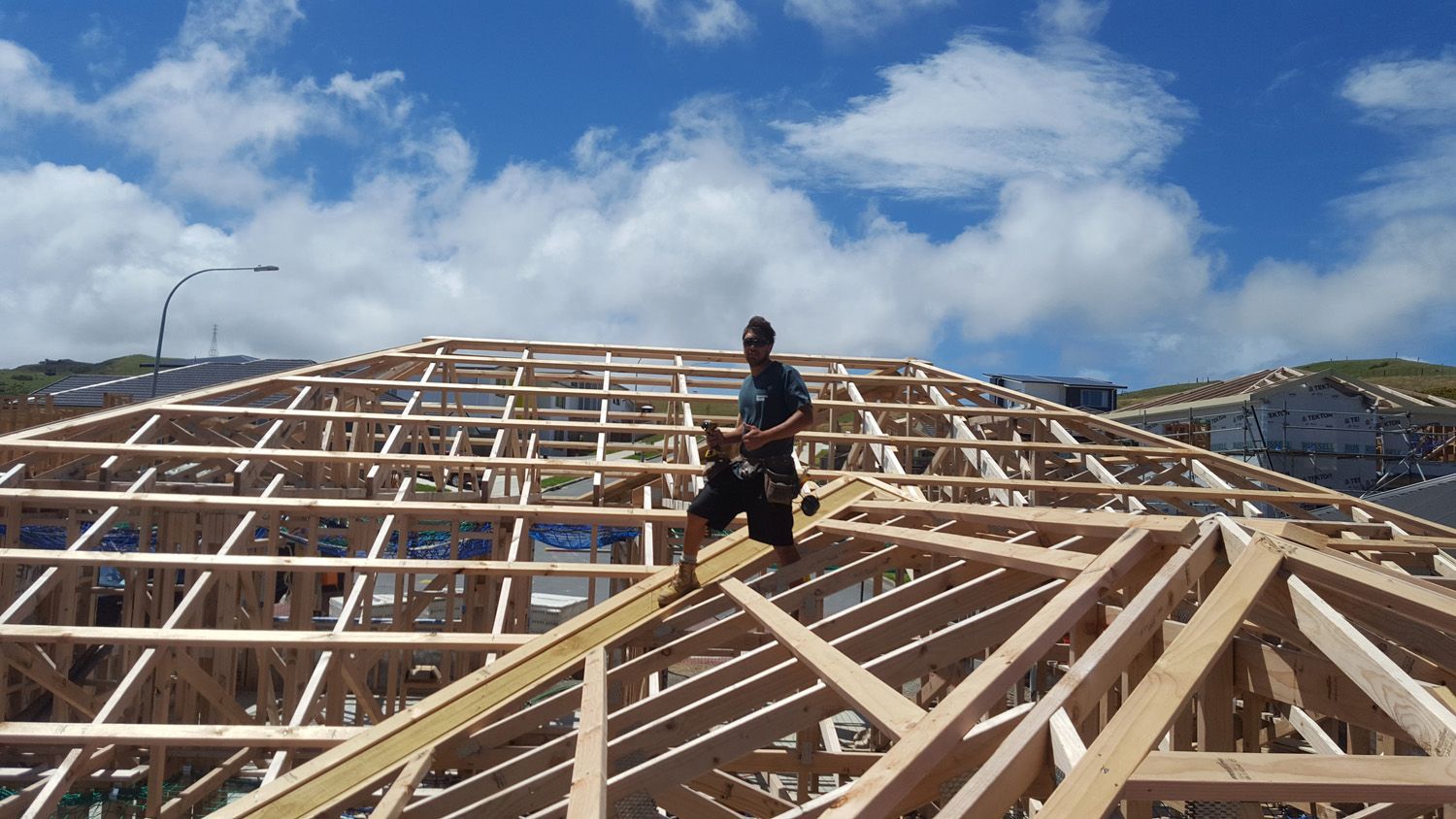 Construction worker on a wooden roof frame under a blue sky, building a house.