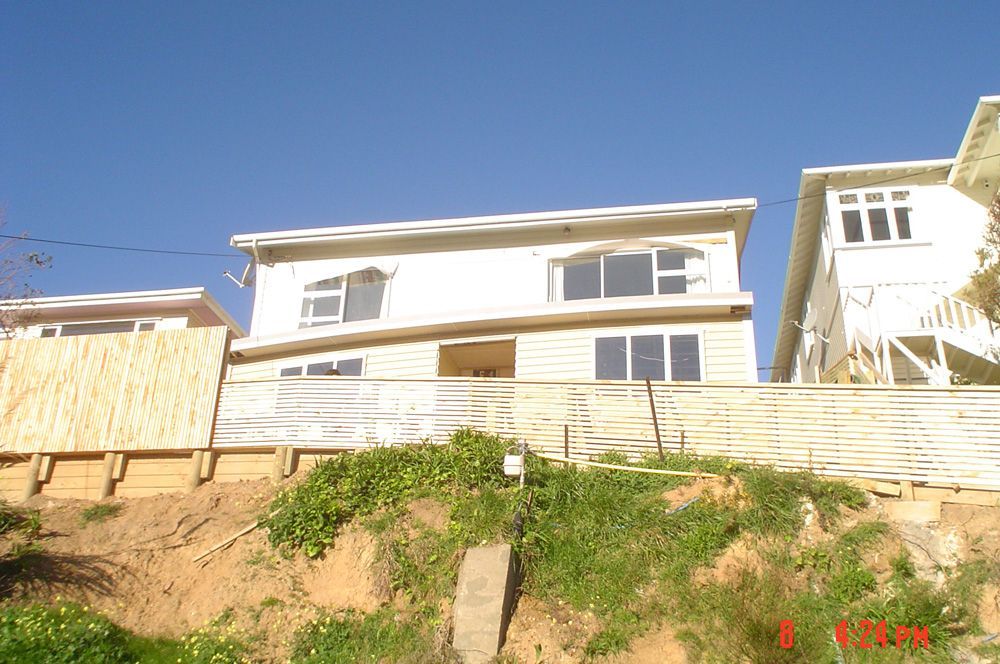 White houses on a hill with a retaining wall. Blue sky overhead, sunny day.