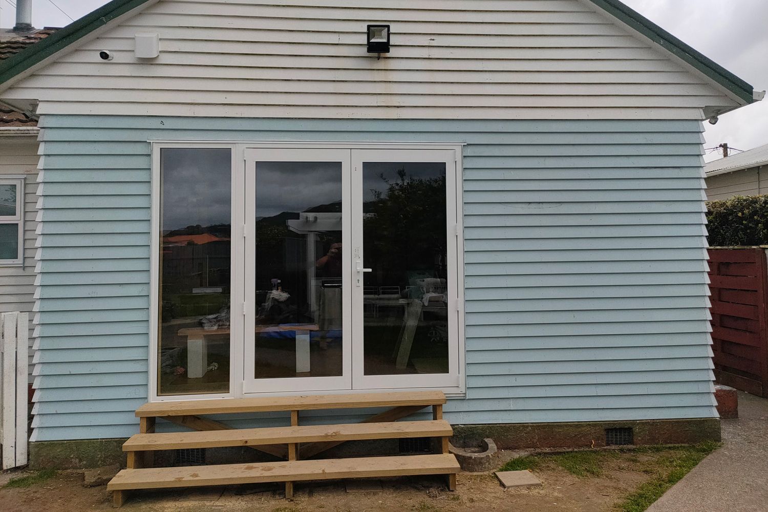 Light blue clapboard building with white-framed glass doors and wooden steps.