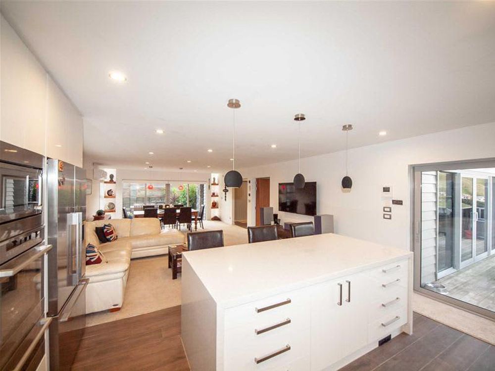 Modern kitchen with white island, stainless steel appliances, and open layout to living area.