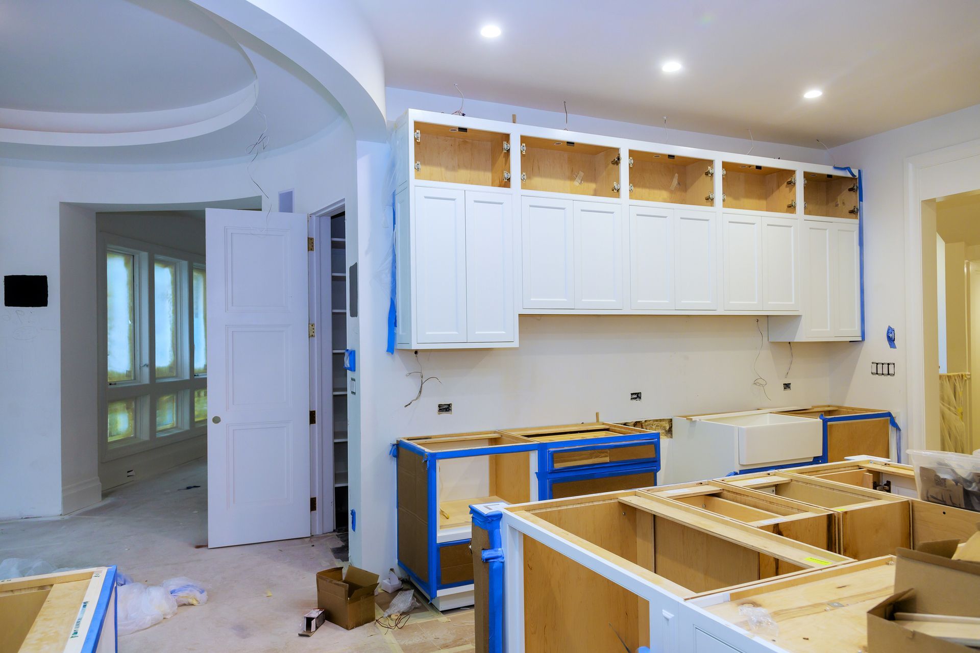 Kitchen renovation: White cabinets installed, lower cabinets awaiting countertops, walls painted, blue tape visible.