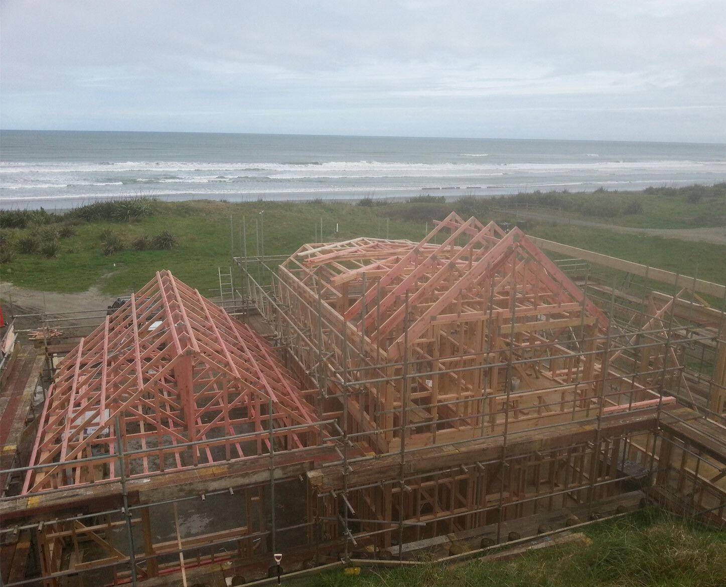 House under construction with exposed wooden framing, beach and ocean in background.
