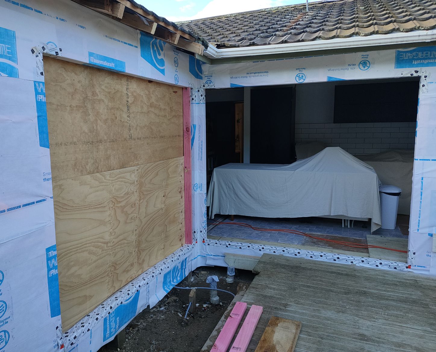 Exterior building under construction, plywood covers window opening, doorway reveals interior.