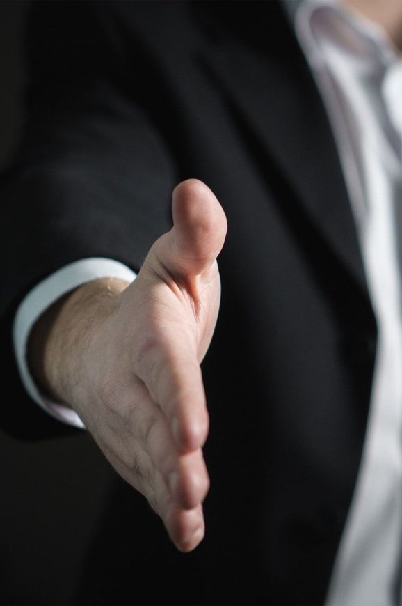A man in a suit is reaching out to shake someone 's hand.