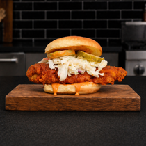Fried chicken sandwich with pickles and slaw on a wooden board in a kitchen