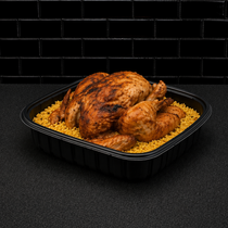 Roasted whole chicken in a black tray on a bed of yellow rice, against a dark tiled background