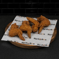 Fried chicken tenders on a paper-lined wooden tray against a dark background.