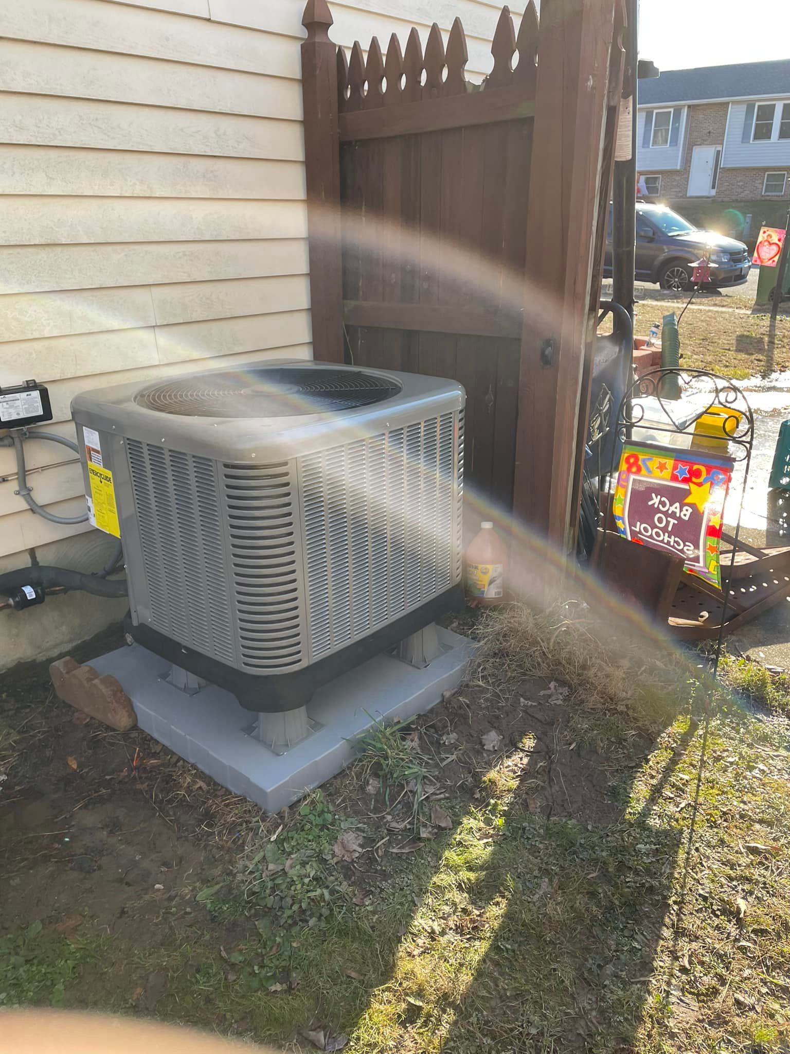 An air conditioner is sitting on the side of a house next to a fence.