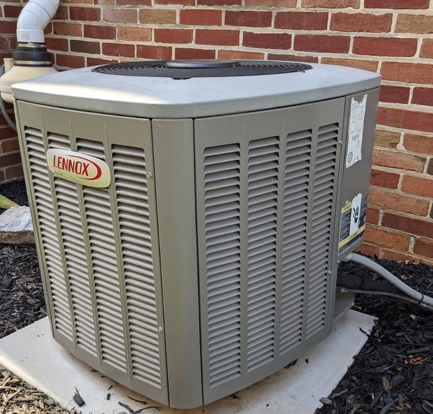 A lennox air conditioner sits in front of a brick wall