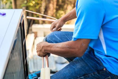 A man in a blue shirt is working on an air conditioner.