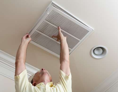 A man is looking up at a vent on the ceiling.
