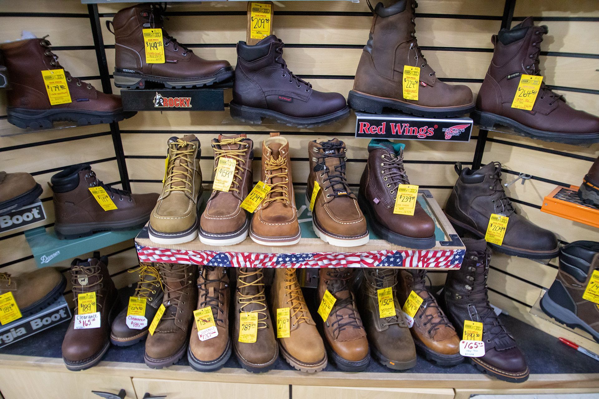 Rows of hiking boots and work boots on display shelves with yellow price tags in a store