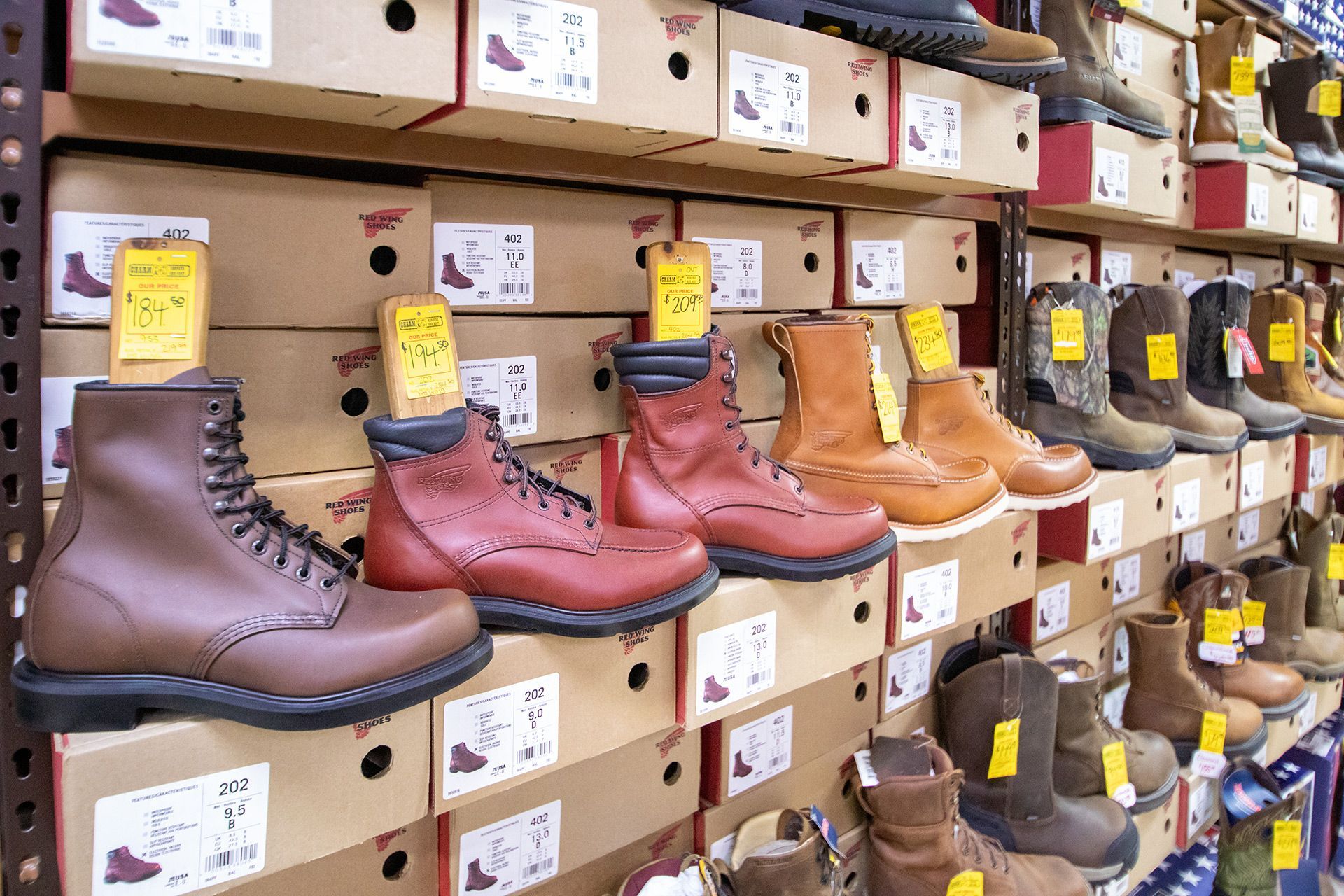 Boots displayed on store shelves in brown, red, tan, and black with yellow price tags.