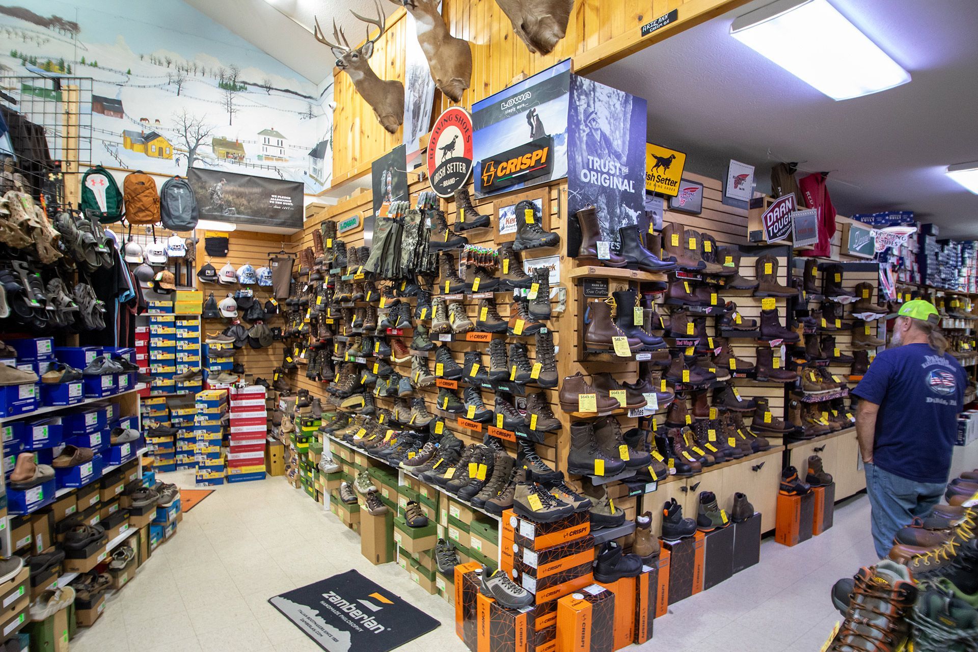 Indoor shoe store aisle with shelves of boots and hiking shoes, and a person browsing on the right