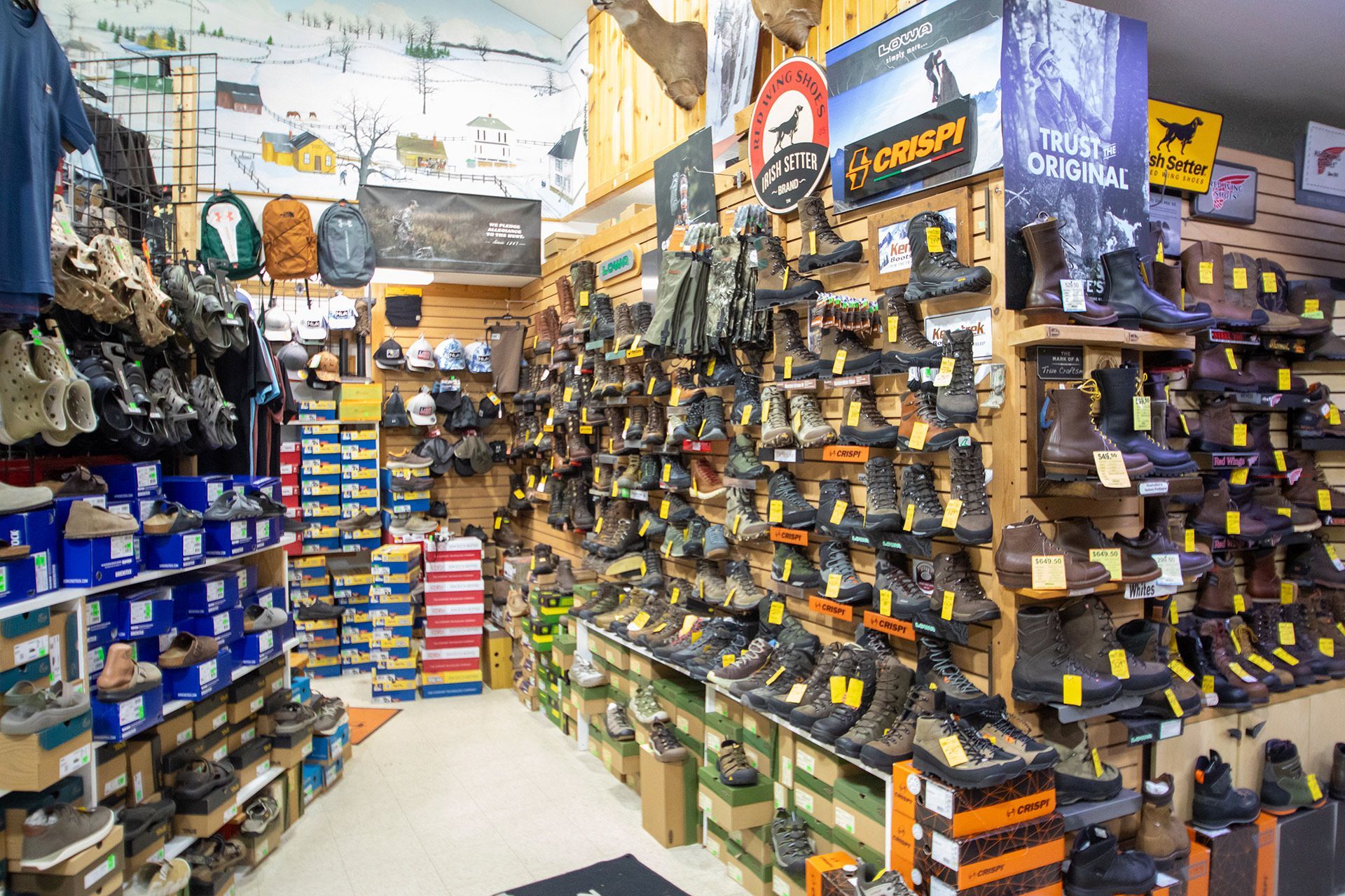 Inside a shoe store aisle with rows of boots and shoes on shelves and stacks of boxes throughout the shop.