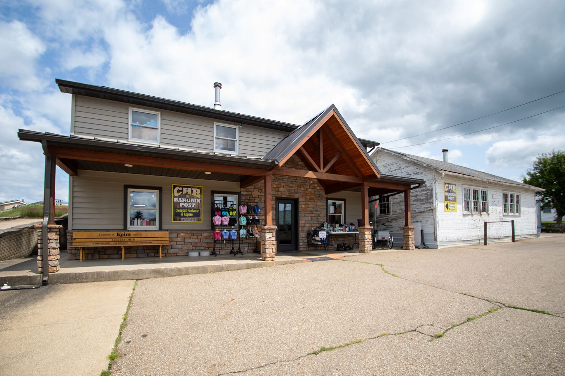 Small rustic building with covered porch and cloudy sky, viewed from a gravel parking lot