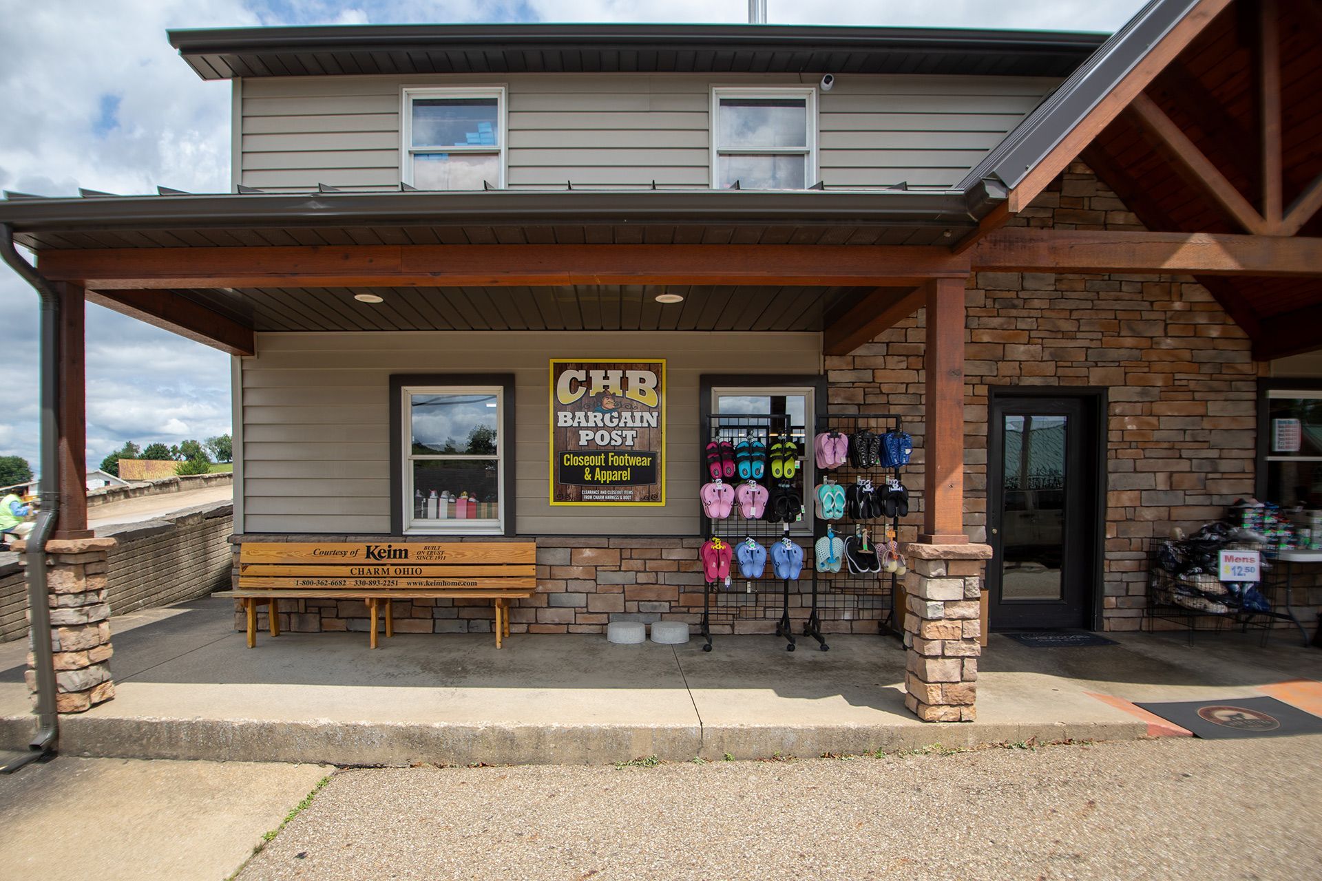 Stone storefront with wooden porch, benches, and hanging souvenir display under a covered roof.