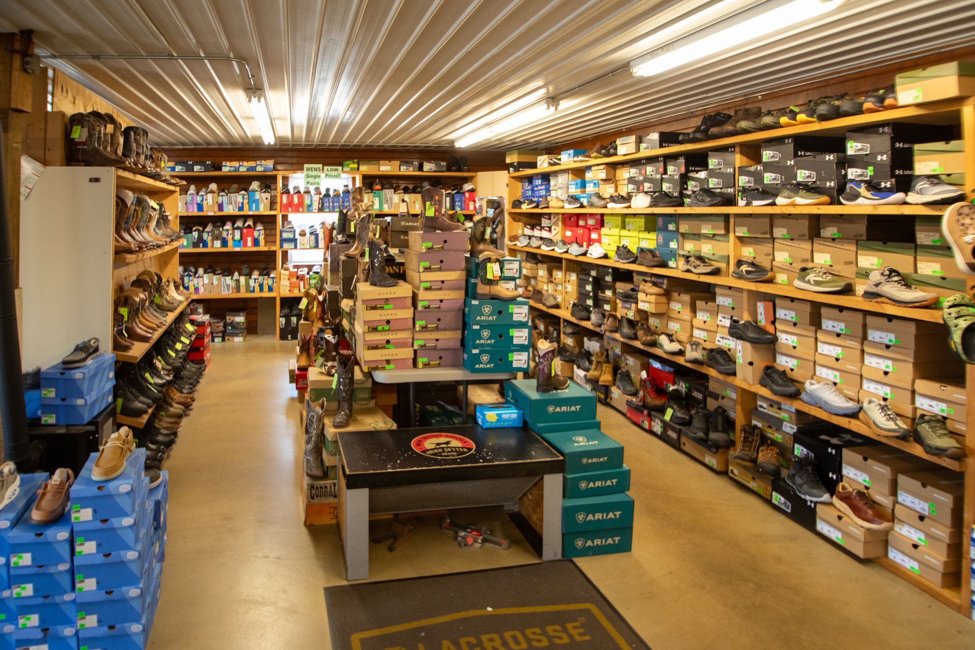 Small grocery store aisle with shelves of packaged goods and produce boxes under bright fluorescent lights