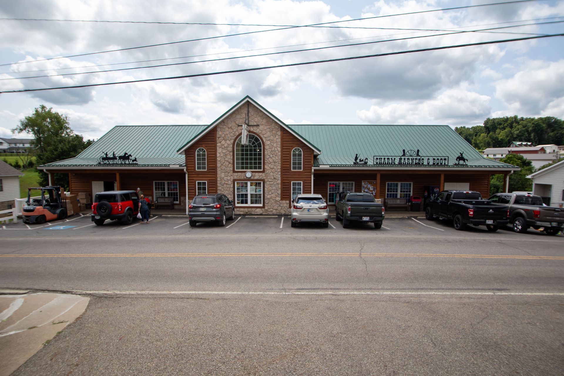 Brick storefront with green roof and parked cars along a road under cloudy skies